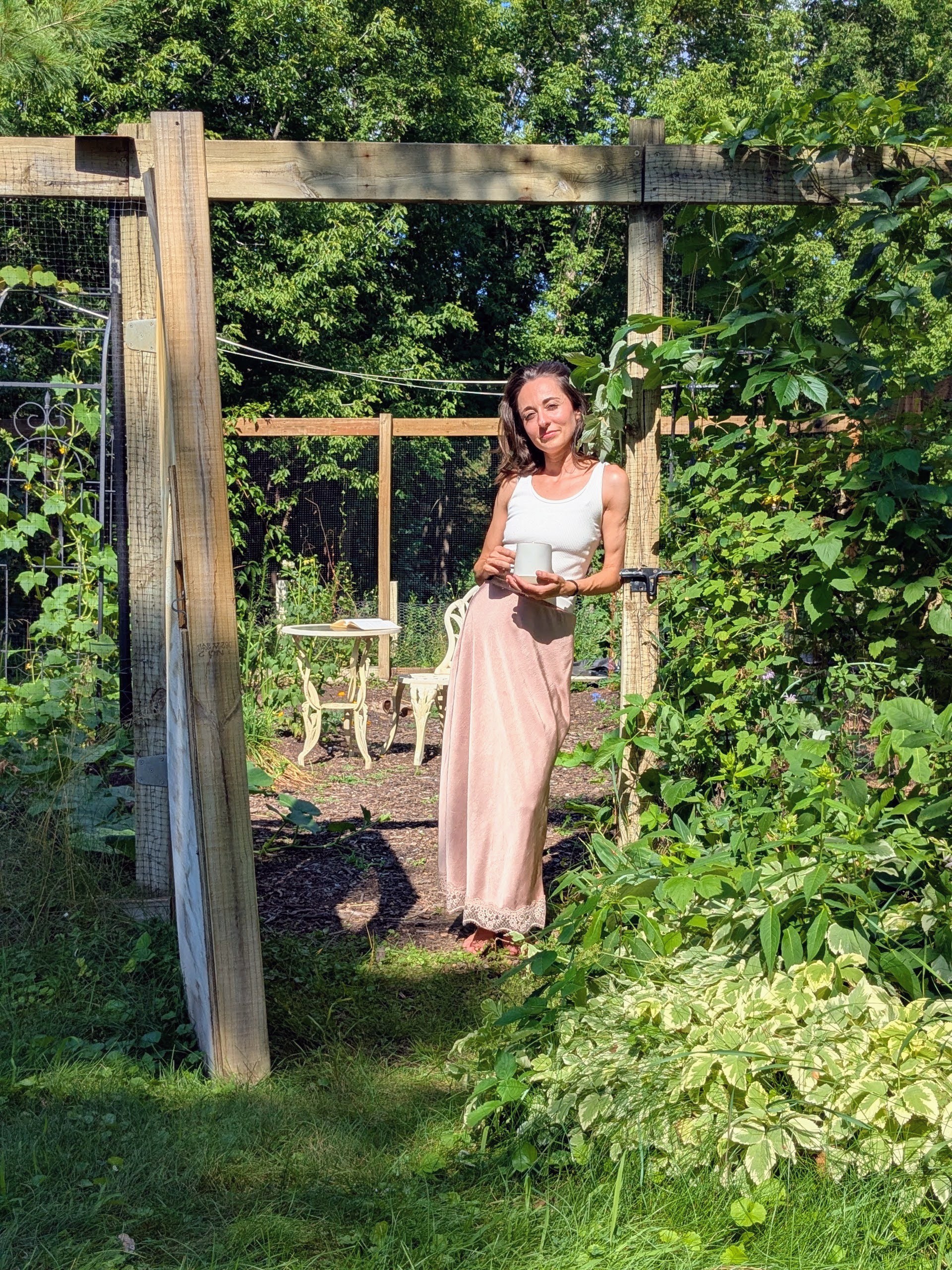 Sanja standing in her garden holding a mug.